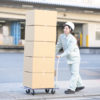 屋外でダンボール箱を台車に載せて運ぶ作業服の女性